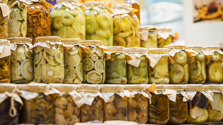 Rows of glass jars with cloth lids full of various pickled vegetables