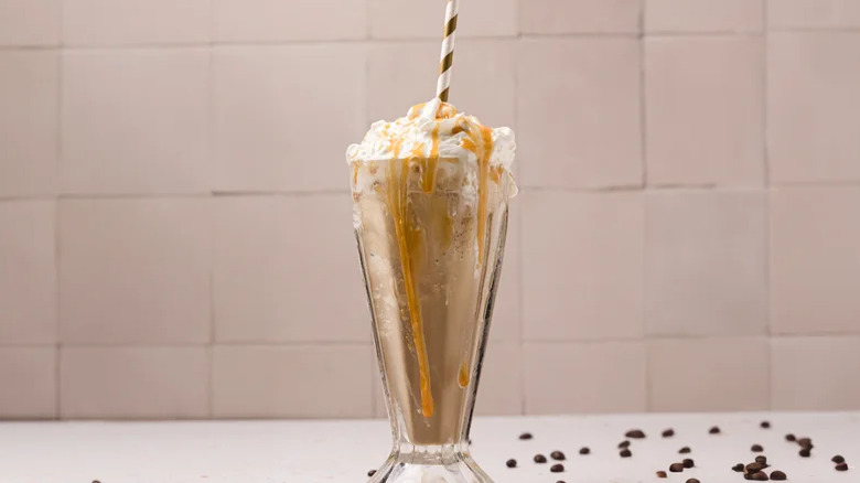 DIY Creamy McDonald's Caramel Frappe in a tall milkshake glass with whipped cream against a pastel background