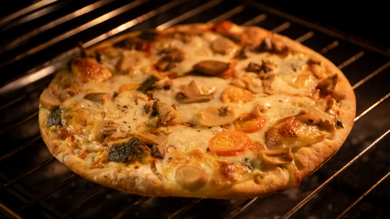 Frozen pizza with mushroom and vegetable toppings, turning golden brown in an oven