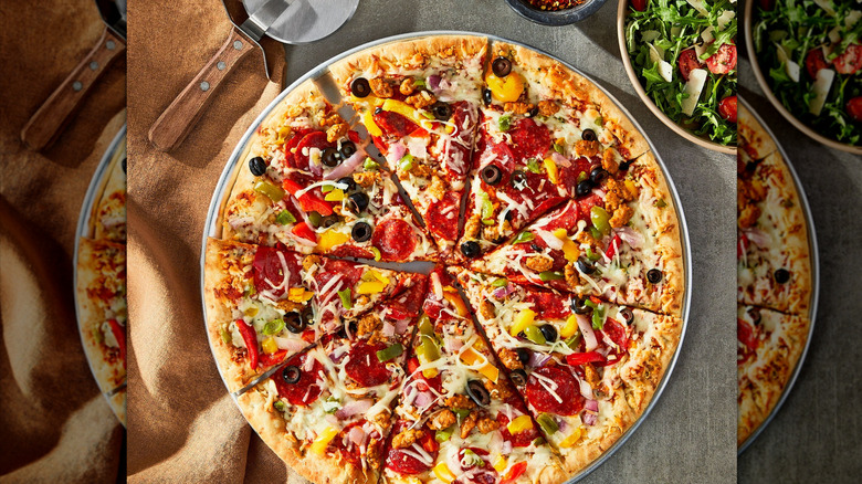 image of a Marketplace deluxe pizza, fresh from the oven, with a pizza cutter visible at top left and a side salad at top right