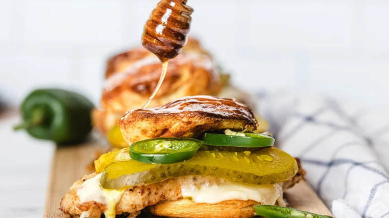 Honey drizzling onto Hot Honey Chicken Biscuit Sandwich on wooden board