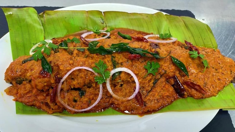 Meen pollichathu served on banana leaf and topped with onions, cilantro, curry leaves, and chile peppers