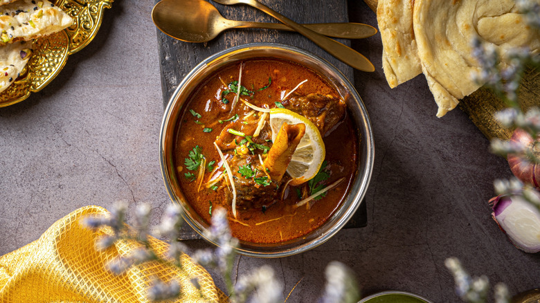 Top view of nihari gosht in bowl, served alongside paratha and two spoons