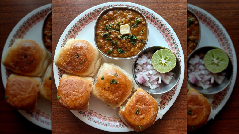 Several bread rolls on plate alongside bowl of mashed vegetables and bowl of onions and lemon