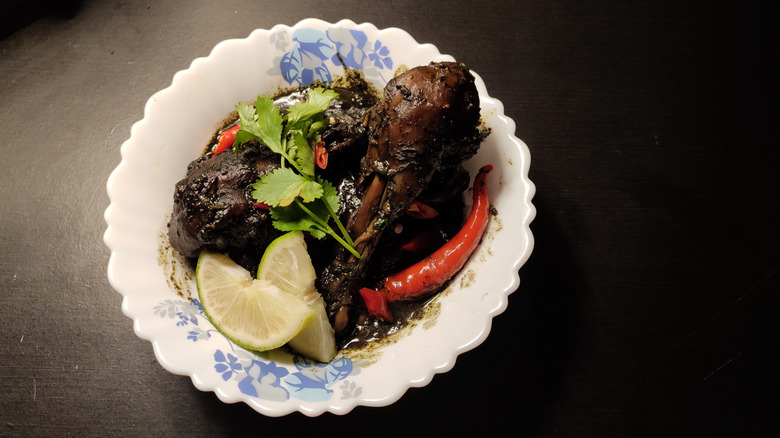 Til diya mangsho served in bowl alongside lime wedges and red chile pepper