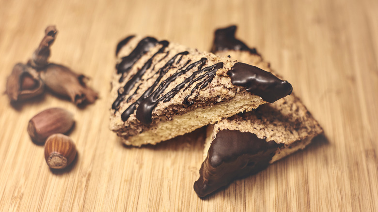 Two nussecken dipped and drizzled with chocolate alongside raw hazelnuts