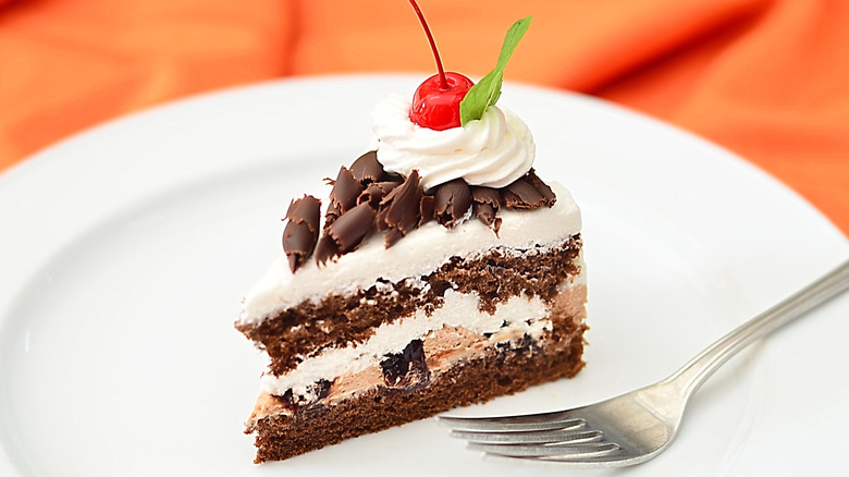 Slice of schwarzwälder kirschtorte topped with cherry and mint on plate with fork