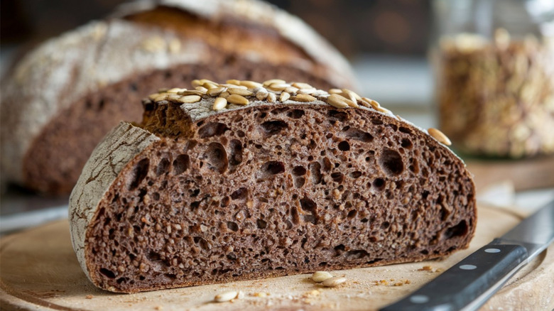 Vollkornbrot loaf topped with seeds on wooden cutting board with knife