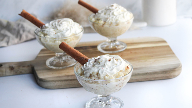 Rice pudding in serving glasses, topped with whipped cream and cinnamon sticks