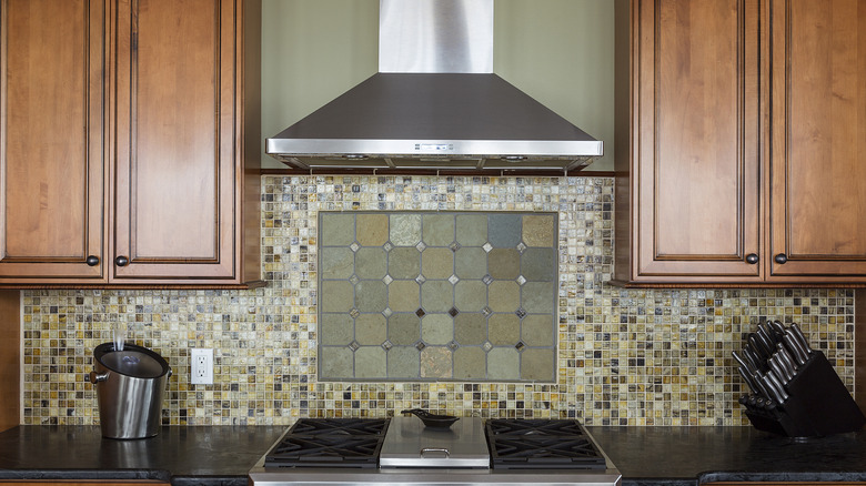Green and brown toned kitchen backsplash with small tiles surrounding a central tile design.