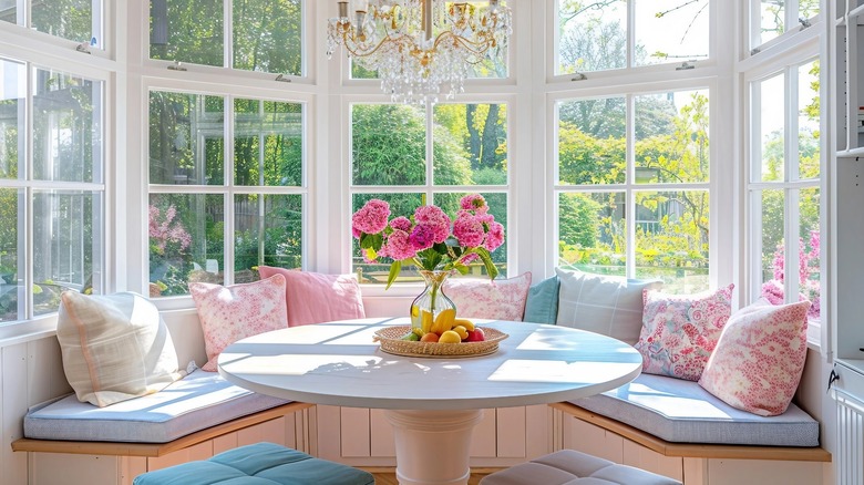 Bright kitchen breakfast nook with bench seating and eight pillows, with flowers and fruit in the center of the table.