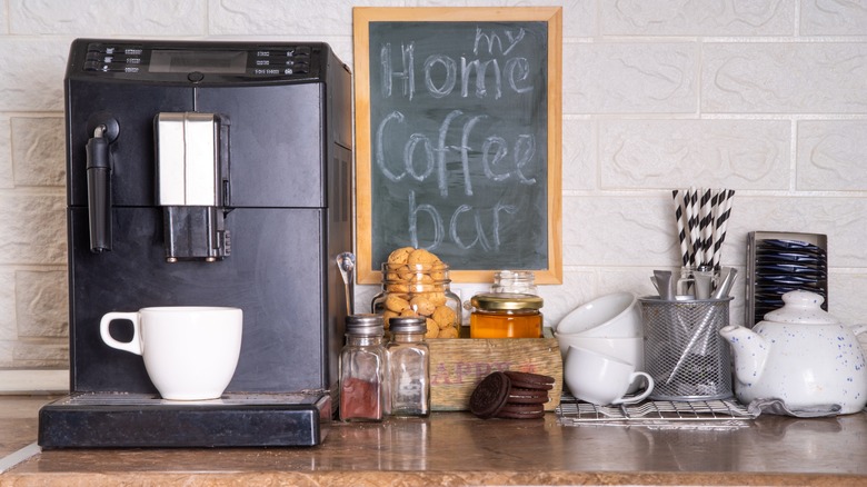 A home coffee bar with a coffee maker and various utensils and supplies next to it.