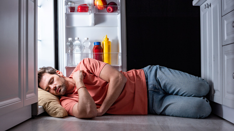 Man asleep in front of open fridge.