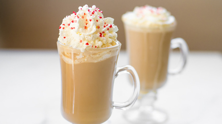 Two mugs of white chocolate mocha, topped with whipped cream and sprinkles