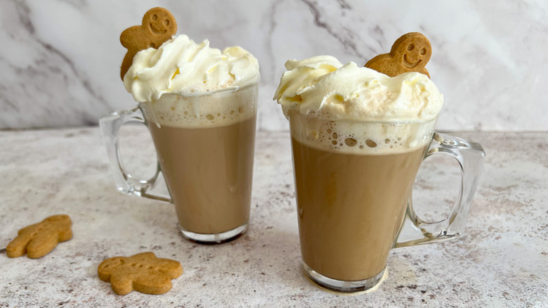 Two mugs of gingerbread latte, topped with whipped cream and gingerbread cookies