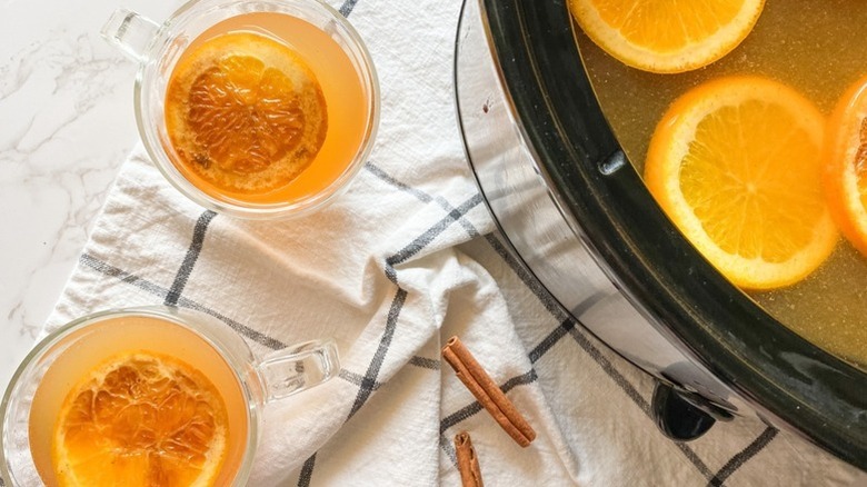 Mulled cider served from slow cooker in to glasses, with orange rounds
