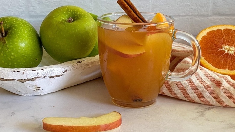 Apple cider in glass mug with cinnamon stick and apples slices