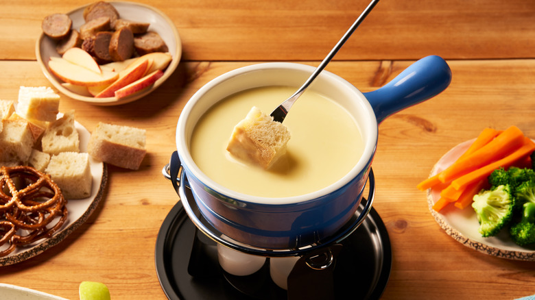 Bowl of Swiss cheese fondue in a blue bowl over flames surrounded by dipping items