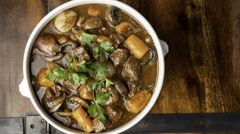 French beef stew in a white dish on a rustic wooden table