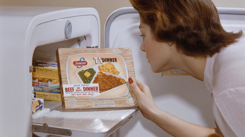 A woman examines a TV dinner box she has taken from the freezer