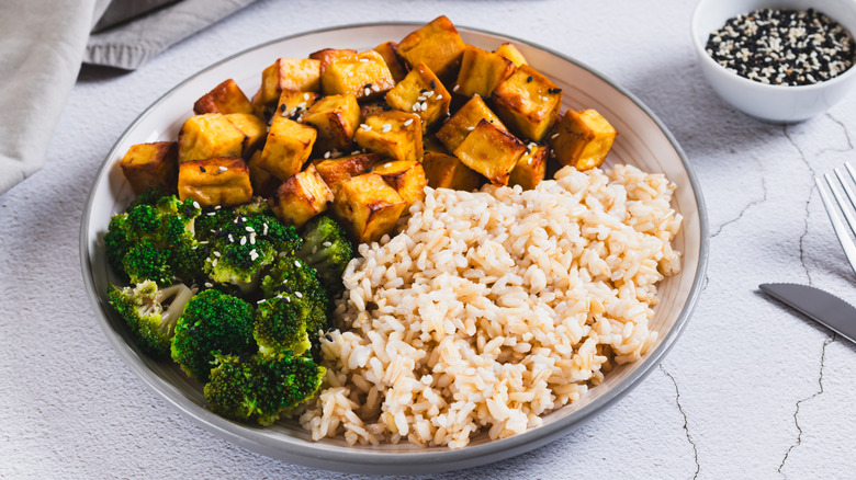 A plate of rice, fried tofu and broccoli on a white table