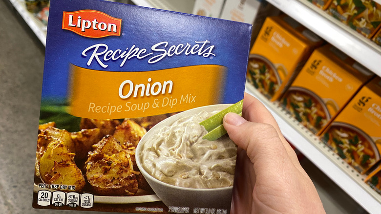 Hand holds up a box of Lipton brand Recipe Secrets Onion soup and dip mix in grocery store