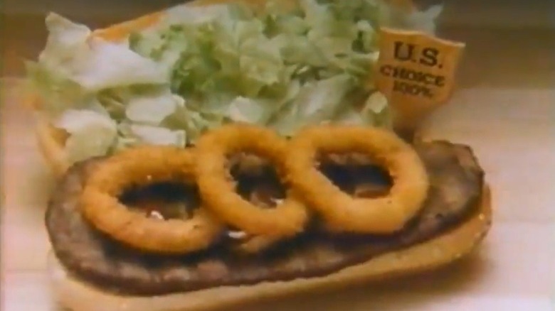A Burger King chopped beefsteak sandwich, open face, featuring onion rings on top of the steak on one side of the bun and lettuce on the other with a small wooden tag that says U.S. Choice 100%