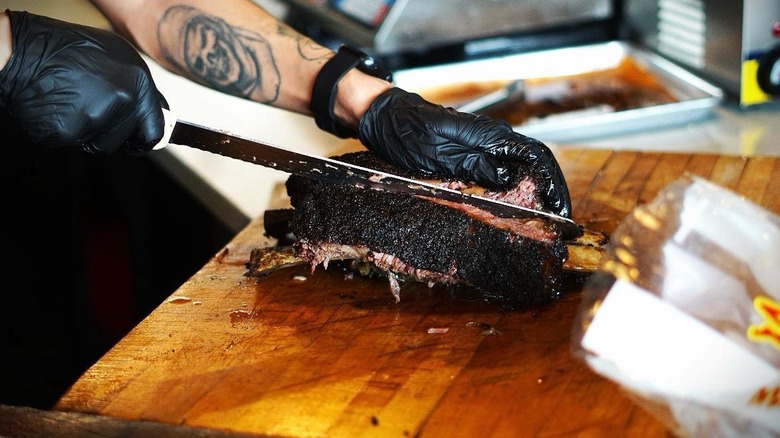 Someone using a knife to slice a brisket on a wooden cutting board