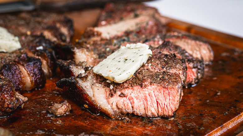 Sliced picanha steak with dab of garlic butter on cutting board