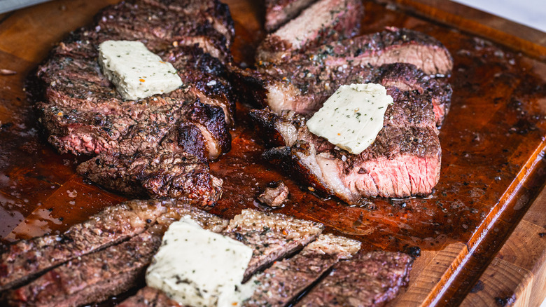 Sliced picanha steak with dab of garlic butter on cutting board