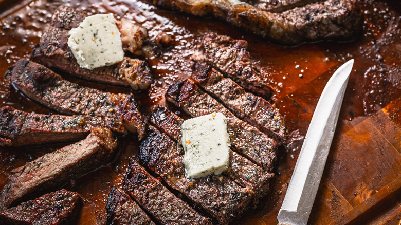Sliced picanha steak with dab of garlic butter on cutting board with knife