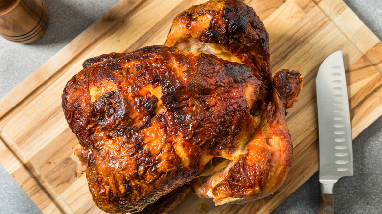 rotisserie chicken on a wooden cutting board with a chef's knife nearby.
