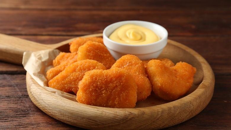 chicken nuggets on a wood plate with a small white ceramic bowl of sauce, all on a wooden tabletop.