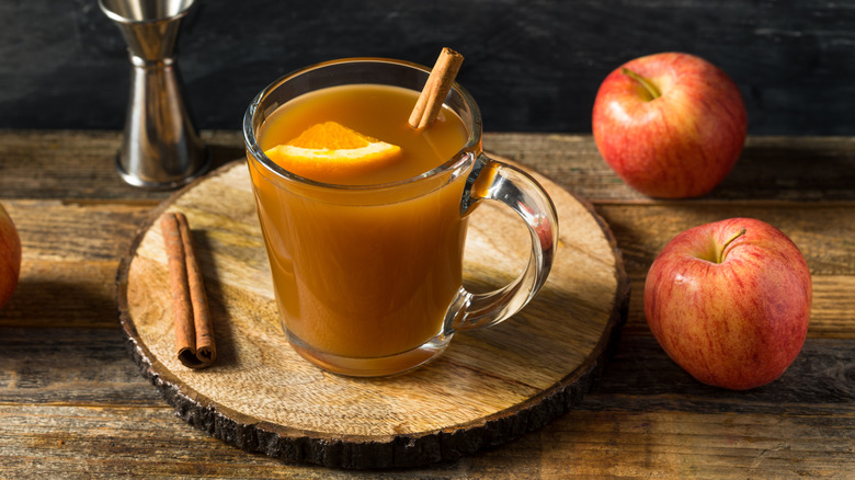 Glass of apple cider on wooden table next to whole apples