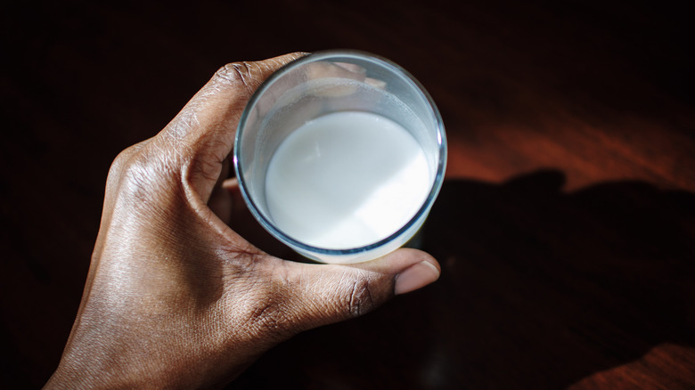 Person's hand holding glass of milk