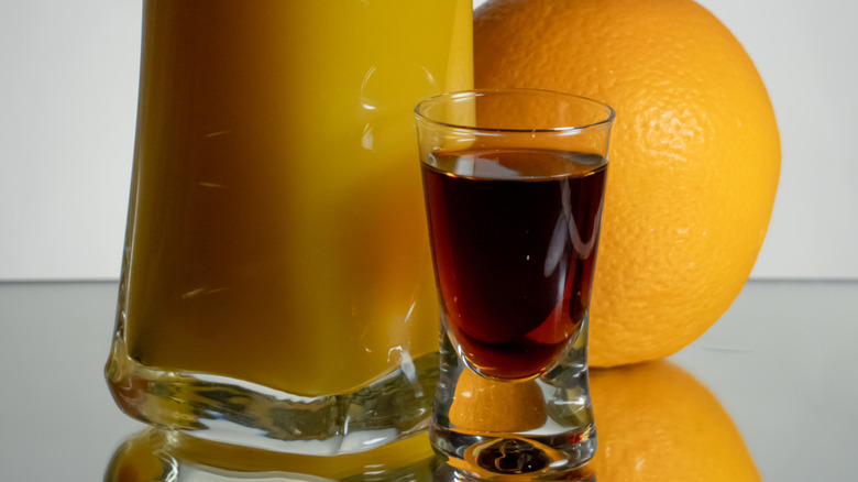 A shot of Jägermeister with a jar of orange juice and a whole orange behind it