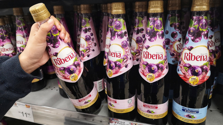 A person's hand grabbing a bottle of Ribena from a store shelf
