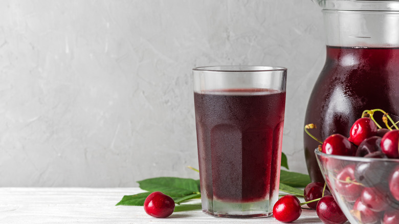 A glass and pitcher of cherry juice with whole cherries on the side
