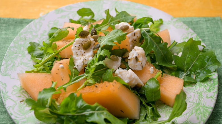 Melon arugula salad on a green and white floral plate