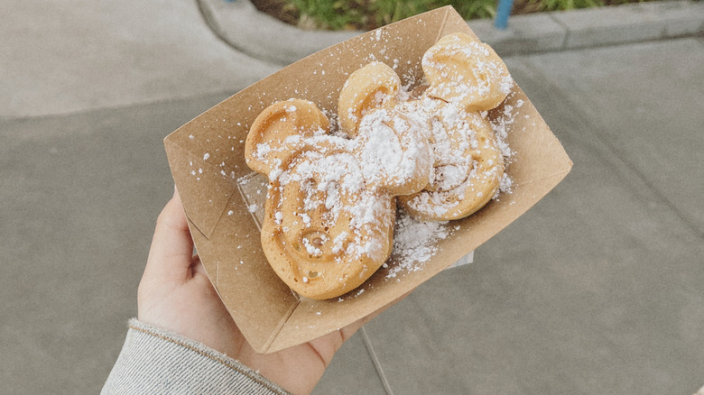 Hand holding Mickey-shaped waffles in a brown container