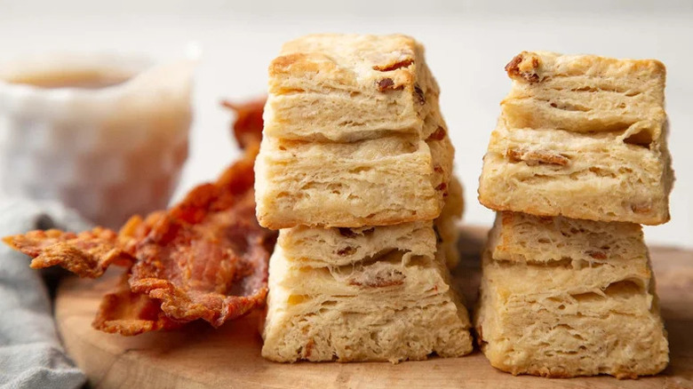 Extra Flaky Maple Bacon Biscuits stacked on wooden board with bacon strips