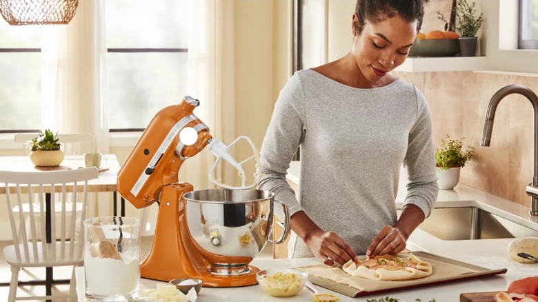 A woman cooks in a kitchen with a honey-colored mixer