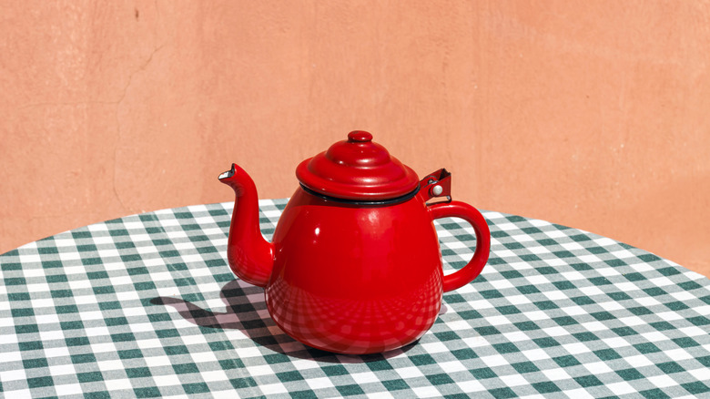 A bright-red kettle on a checkered tablecloth
