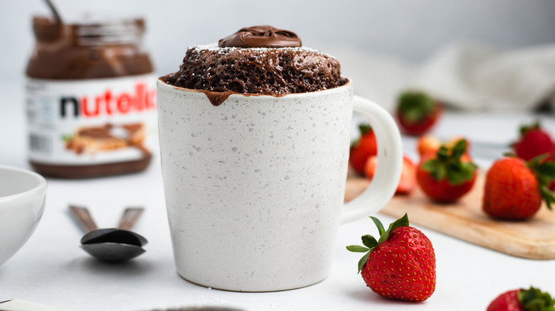 Nutella mug cake in grey speckled mug next to fresh strawberries