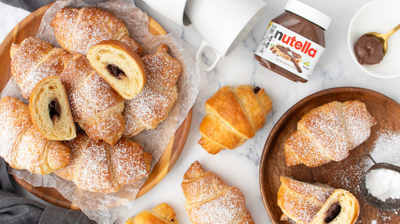 Pile of Nutella-stuffed croissants on two serving plates, dusted with powdered sugar