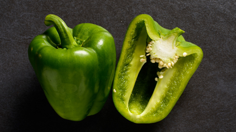 An intact green bell pepper next to a cut one, with the seeds inside being shown