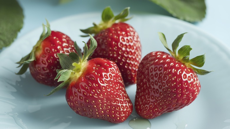 A close-up of four strawberries on a plate, showing the seeds on the outside