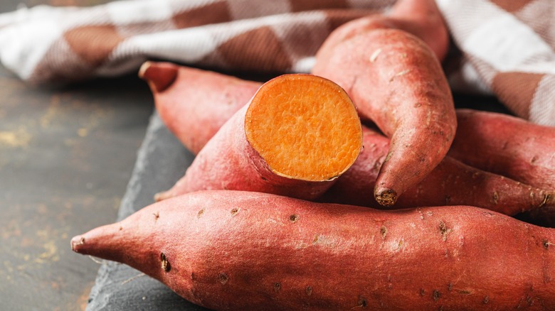 A collection of sweet potatoes with one being cut and others showing their narrow ends