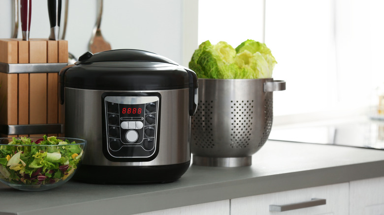 Slow cooker on kitchen counter, between a salad and a colander with lettuce