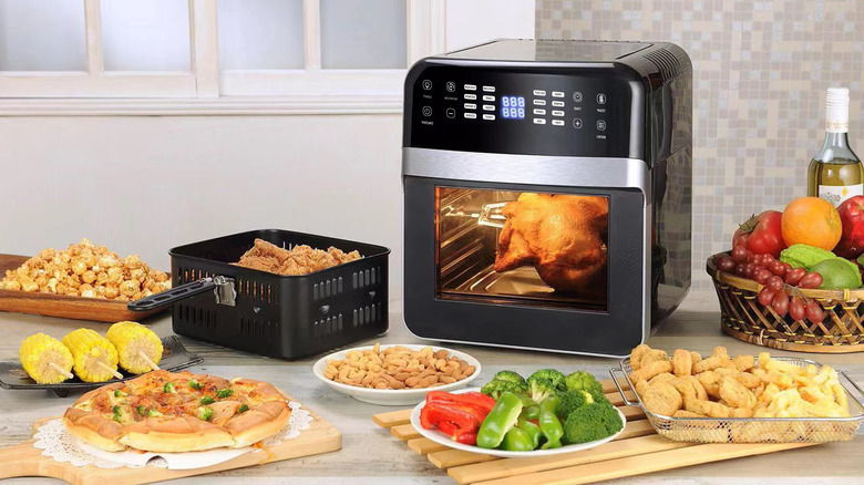 Air fryer on a counter, surrounded by air-fried dishes and other foods